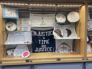 One of the display cases where students embroidered injustice and food sovereignty and images of side profiles, flowers, peace signs, and more.